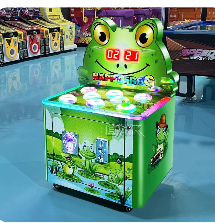 Máquina recreativa con martillo de rana verde iluminada en el suelo de una sala de exposiciones de juegos.